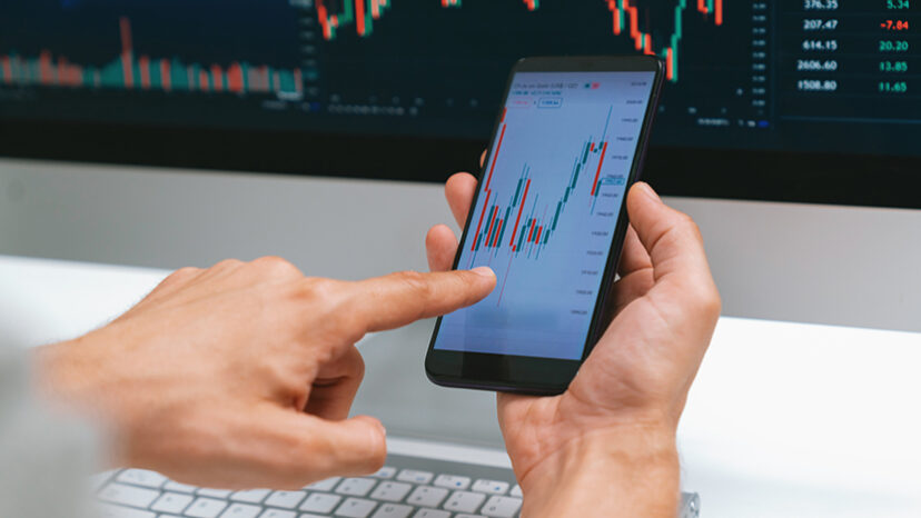 Investors pointing on screen with smartphone with laptop in stock. Pecuniary.