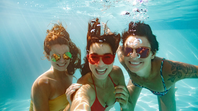Cheerful friends making selfie underwater in pool