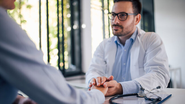 Friendly male doctor holding patient’s hand for encouragement and empathy.