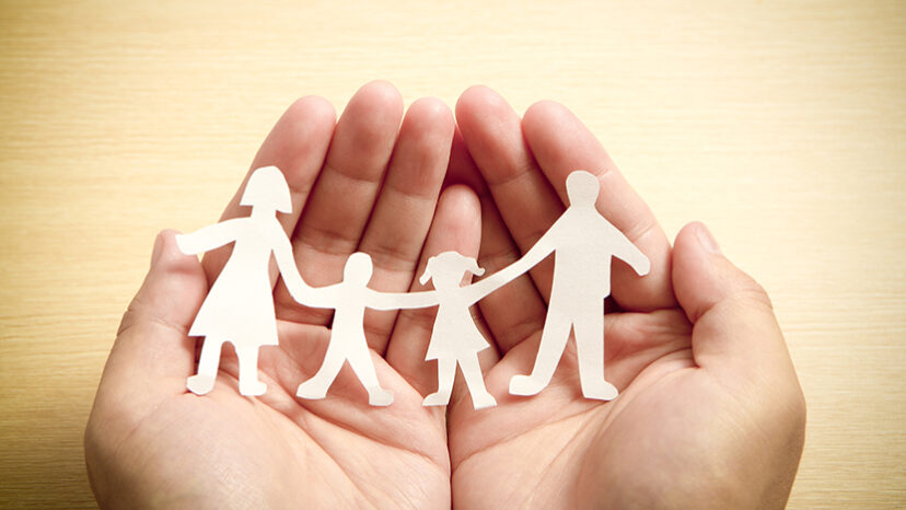 Paper family in hands with wooden texture background