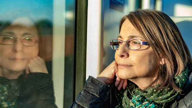 Adult woman with glasses looking through the train window.