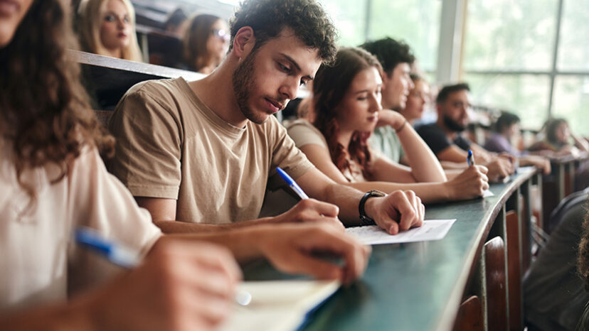 Male college student writing an exam in lecture hall.