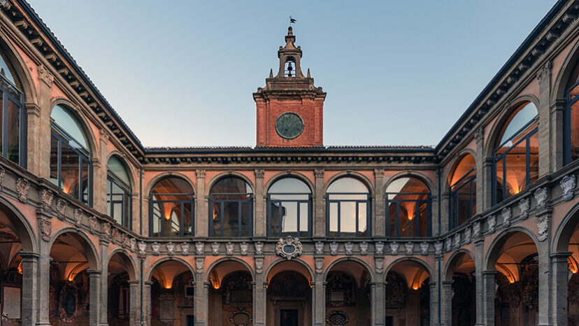 Golden hour light gently kisses the terracotta facade of the University of Bologna, framing the historical main entrance and its clock tower, a portal to centuries of academic excellence